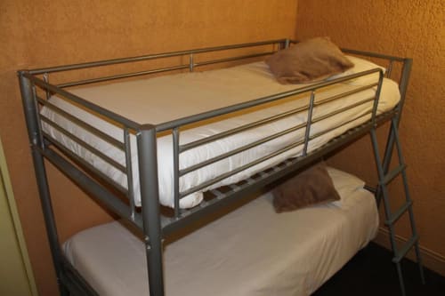 Lit superposé en métal avec matelas blancs et oreillers marron dans une chambre quadruple de l'hôtel Libre à La Vespière, France