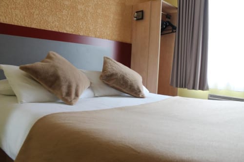 Hotel bed at Libre Hôtel in La Vespière with white linens, decorative pillows, and modern headboard
