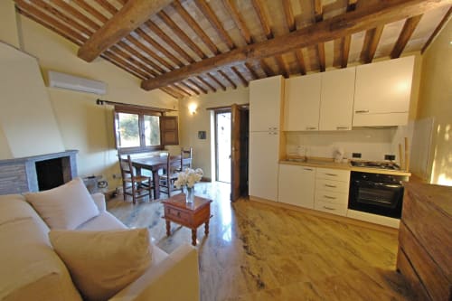Interno luminoso a open-plan del cottage Agriturismo Buriano con cucina color crema, soffitto con travi in legno, camino e sala da pranzo