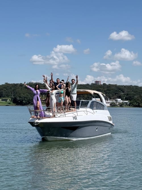 Grupo celebrando em barco no Chales do Lago, Caldas Novas, com vista panorâmica do lago e mata ao fundo