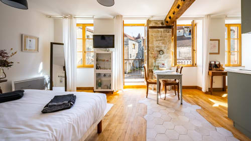 Helles Schlafzimmer in der La Maison George mit Holzböden, mehrere Fenster mit gelben Rahmen mit Blick auf