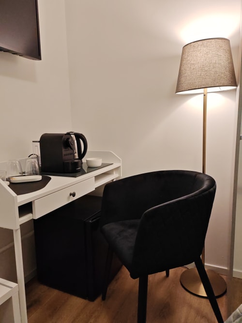 Modern hotel room with black chair, white desk, coffee maker, and floor lamp at Alloggi Tosca Airport Lodge