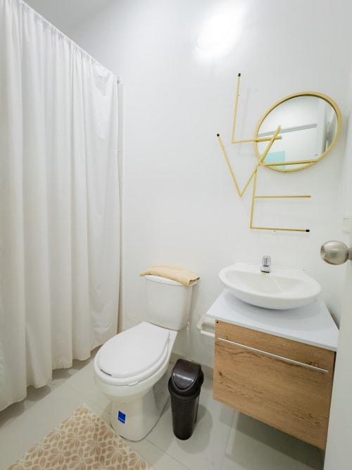 Baño moderno del hotel La Puerta del Ángel en Ricaurte con lavamanos blanco, inodoro y espejo circular dorado