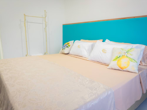 Habitación luminosa en La Puerta del Angel con cabecera turquesa, ropa de cama blanca con almohadas de frutas y colcha crema