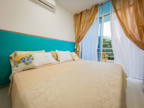 Dormitorio luminoso con pared turquesa, ropa de cama crema, cortinas doradas y balcón con vista al jardín en La Puerta del Angel