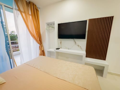 Moderno dormitorio doble con televisión de pantalla plana, muebles blancos empotrados, panel de acentos en madera oscura y acceso a balcón en La Puerta