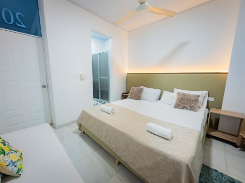 Moderna habitación doble del hotel La Puerta del Ángel en Ricaurte con cama queen, cabecero verde, aire acondicionado, ventilador y baño privado