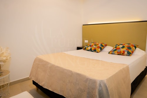 Habitación luminosa en La Puerta del Angel con cama blanca, almohadas coloridas, cabecera amarilla y ventilador en Ricaurte, Colombia