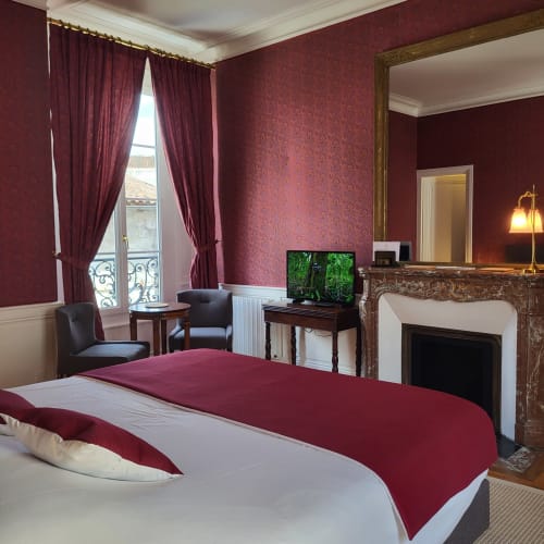 Chambre raffinée bordeaux aux Logis des Tourelles à Cognac avec cheminée et vue sur les fenêtres parisiennes