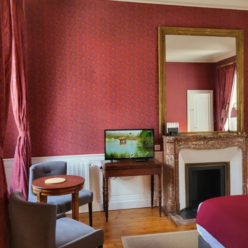 Chambre élégante au Logis des Tourelles à Cognac avec papier peint en damas rouge, cheminée ornementale et mobilier d'époque