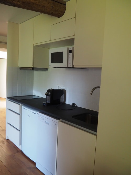 Cozinha moderna com armários amarelos, bancada preta, eletrodomésticos brancos e micro-ondas no apartamento Quinta da Coutada