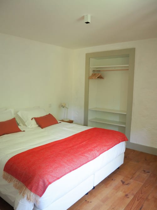 Quarto luminoso com paredes brancas, cama vermelha, piso de madeira e closet embutido na Quinta da Coutada