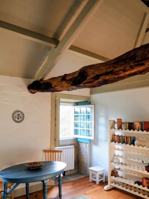 Interior rústico da Quinta da Coutada com vigas de madeira aparentes, mesa de jantar azul e prateleiras flutuantes