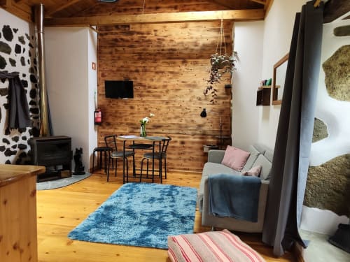 Bright living room at Casa Rosa villa in Fajazinha with wooden ceiling, blue rug, dining table, sofa, and fireplace