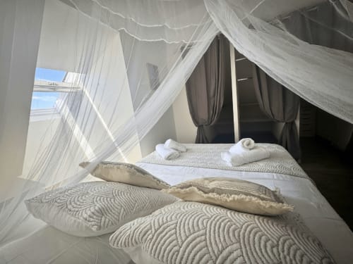Luxurious canopy bed with white sheer drapes and patterned bedding at Horizon Doré hotel in Gourbeyre, Guadeloupe