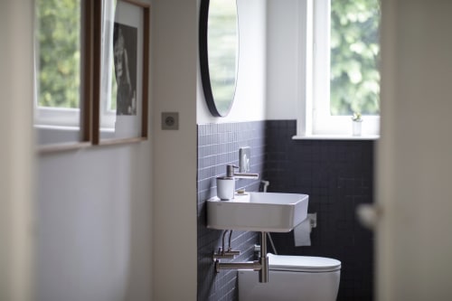 Modern bathroom at Villa Sonneville in Roubaix with black tile accent wall, white sink, and round mirror