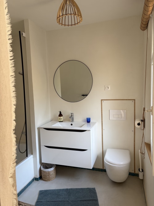 Salle de bain moderne au gîte Le Patio aux Oiseaux à La Ciotat avec meuble blanc, miroir rond et toilettes design