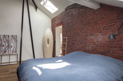 Chambre moderne avec lit bleu, mur de briques rouges apparentes, puits de lumière et décor minimaliste à la Villa Sonneville B&B à Roubaix