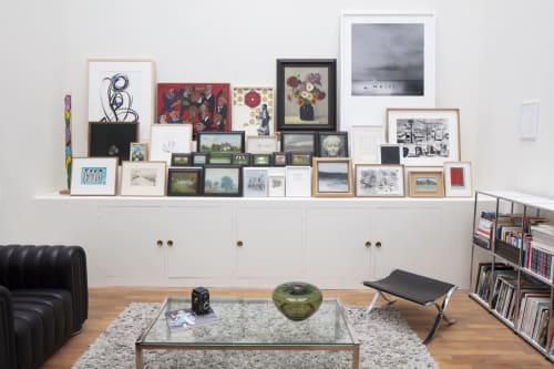 Modern living room at Villa Sonneville B&B in Roubaix with framed artwork shelf, glass coffee table, and black leather