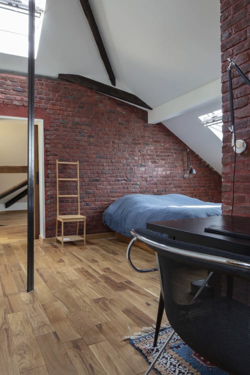 Spacious bedroom with exposed brick walls, bed with blue bedding, wooden floors, and skylights at Villa Sonneville, Roubaix
