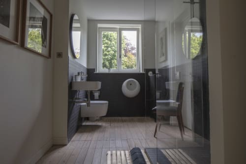 Modern bathroom with black tile walls, white fixtures, toilet with bidet, and garden views through windows at Villa