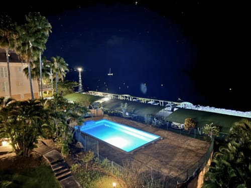 Illuminated pool at Horizon Doré hotel overlooking Gourbeyre coastline at night with palm trees and Caribbean waters
