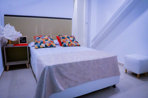 Habitación moderna del hotel La Puerta del Angel en Ricaurte con cama blanca, cojines coloridos y decoración minimalista