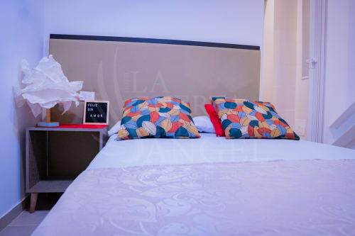 Elegante habitación de hotel en La Puerta del Angel con sábanas blancas, almohadas con patrones coloridos y mesilla de noche con lámpara