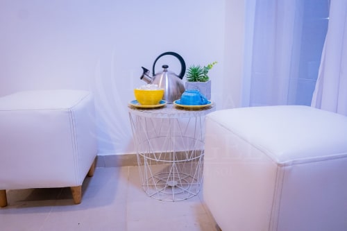 Área de descanso moderna en el hotel La Puerta del Angel con puffs blancos, mesa con cesta decorativa, hervidor y planta en maceta