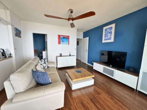 Modern living room at Horizon Doré in Gourbeyre with cream sofa, blue accent wall, flat-screen TV, wooden coffee table, and
