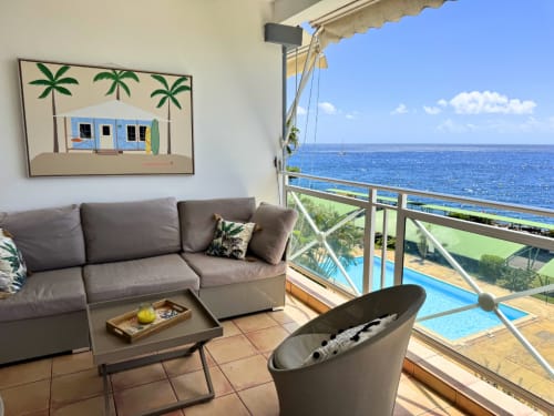 Oceanview balcony at Horizon Doré hotel in Gourbeyre with gray seating, pool, and sea views
