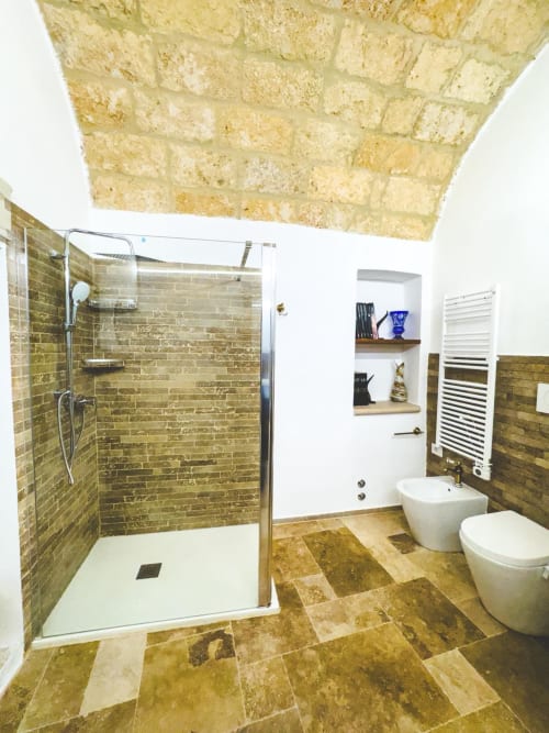 Bagno moderno con pavimentazione in pietra naturale dai toni olivastri, doccia con box in vetro, sanitari bianchi e scaldasalviette termico