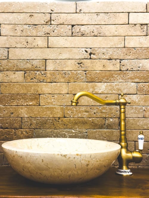 Lavabo in marmo lussuoso con rubinetto in ottone su parete in travertino nell'appartamento Soprano 1 a CorteLirice Paradiso, Italia