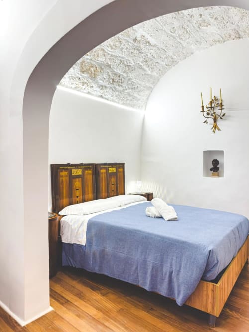 Camera Soprano 1 a CorteLirice Paradiso con soffitto a volta, letto in legno, biancheria blu, candelabro in ottone e pareti imbiancate