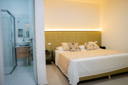 Habitación 103 del hotel La Puerta del Angel con cama doble, cabecera dorada, baño privado y comodidades modernas en Ricaurte