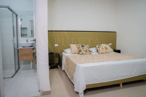 Habitación moderna en La Puerta del Angel con cama doble, sábanas blancas, cabecero oliva y baño privado en Ricaurte