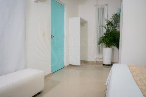 Pasillo moderno de hotel en La Puerta del Angel con puerta turquesa, banco blanco, planta decorativa y diseño minimalista