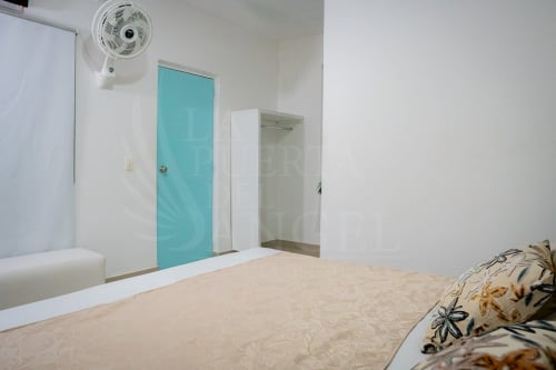 Dormitorio luminoso en hotel La Puerta del Angel en Ricaurte con cama, puerta turquesa, ventilador y espacio de armario