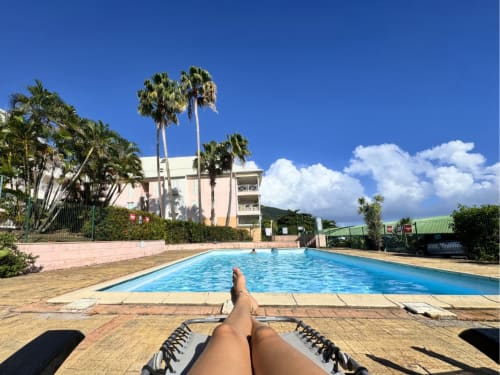 Guest relaxing poolside at Horizon Doré hotel in Gourbeyre, Guadeloupe, with palm trees and mountain views