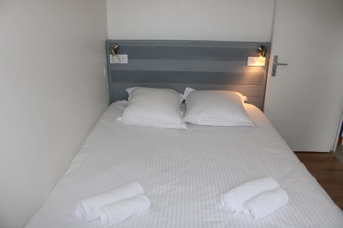 Cozy bedroom at Domaine des Piéris cottage with striped bedding, white pillows, and rolled towels in Grandcamp-Maisy