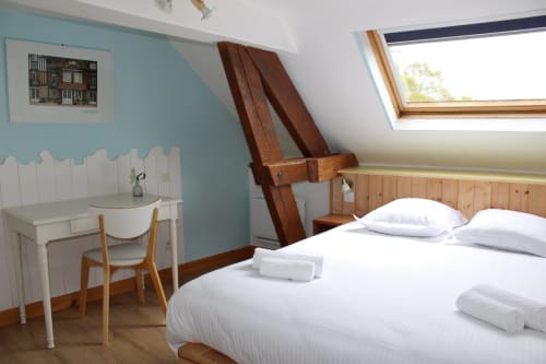 Bright attic bedroom at Domaine des Piéris with white bed, turquoise walls, skylight, wooden desk, and garden views in