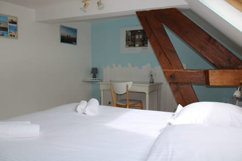 Bright attic bedroom at Domaine des Piéris with white bedding, wooden beams, blue accent walls, desk, and garden view in