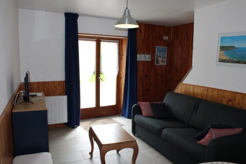Comfortable living room with dark sofa, wooden furnishings, and garden view at Domaine des Piéris cottage in Grandcamp-Maisy
