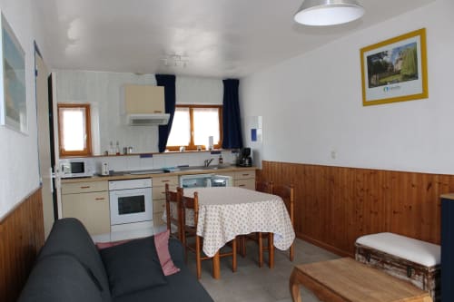 Cozy kitchen-living area in Grandcamp-Maisy cottage with wooden paneling, dining table, and garden view windows