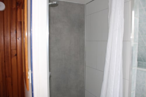 Modern shower area with gray tile walls and white curtain at Domaine des Piéris cottage in Grandcamp-Maisy