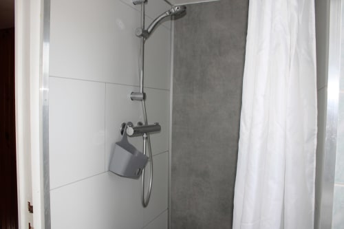 Modern shower with black fixtures and white tile in Domaine des Piéris cottage bathroom in Grandcamp-Maisy
