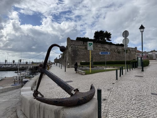 Vista da marina à beira-mar com fortaleza de pedra histórica e âncora, Ribeirinha Portugal