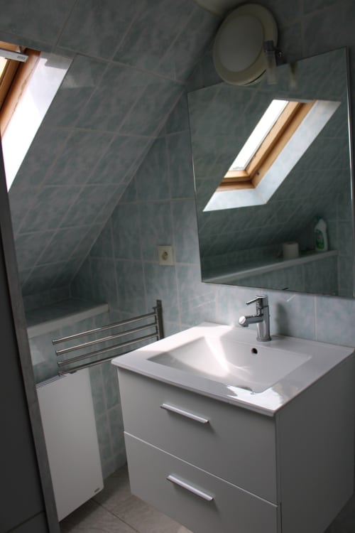 Modern bathroom in Grandcamp-Maisy cottage with white sink vanity, gray tiled walls, skylight windows, and heated towel rack