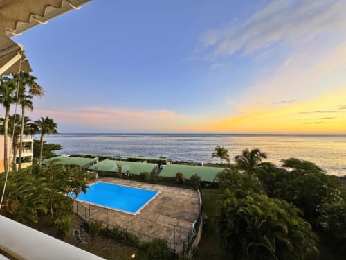 Horizon Doré sunset view from Gourbeyre with blue pool, palm trees, and Caribbean ocean at dusk