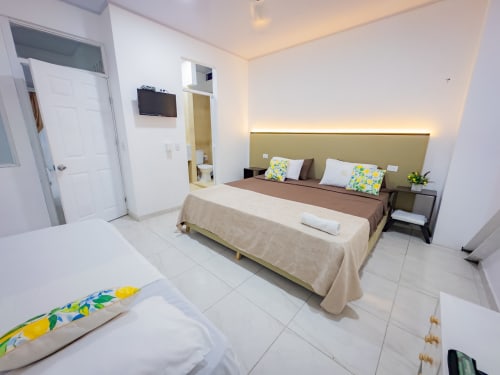 Habitación triple moderna del hotel La Puerta del Angel en Ricaurte con dos camas, televisor de pantalla plana y mobiliario contemporáneo